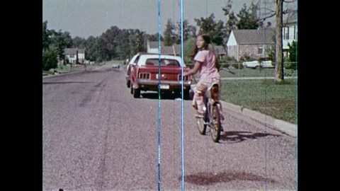 1970s: Children ride bikes single file down street, ride around parked cars. Boy Stock Footage