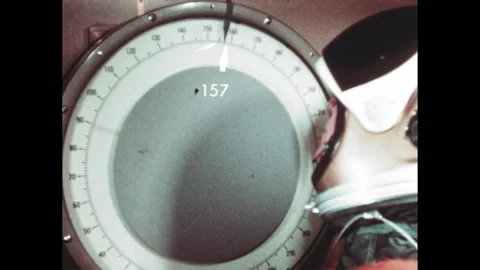 1970s: Elevator doors close. Astronaut watches arrow on scale decrease. Text Stockbeeldmateriaal 270368702