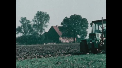 1970s: field of dry grass blows in wind near farm fields, tractor in field pulls Stock Footage 292805183