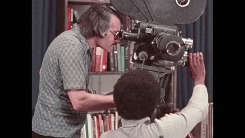 1970s: Film crew adjusts camera.  Woman types.  Woman flips through pad of Stock Footage 220431086