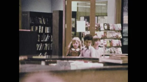 1970s: Flyers, pamphlets on wall in library. Three kids talk to woman behind 库存影片 159987085