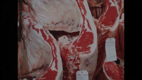 1970s: Fork stabs steak.  Cuts of beef hang.  Grocery store.  Butcher hands meat Stock Footage 162328281