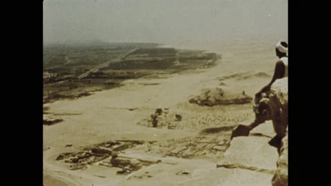 1970s: High angle, men climbing rocks. View of desert, man sitting on pyramid in Vidéo 155855371