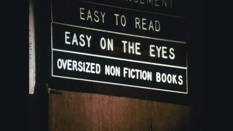 1970s: librarian sorting over-sized, non-fiction books, man reading an Stock Footage 119503863
