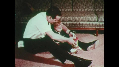1970s: Living room, baby boy sits on floor in front of couch with father, plays Stock Footage