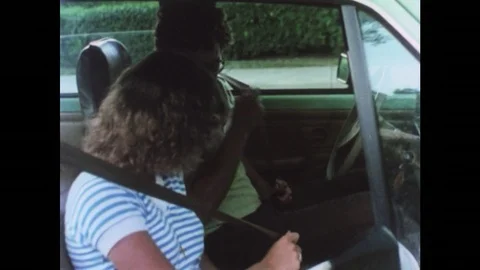 1970s: Man and woman put on seatbelts. Car drives on road. Stop at yellow light. Stock Footage