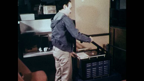 1970s: Man braces scanner over book, puts on headphones at desk and turns knobs 스톡 동영상 86774672