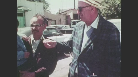 1970s: Man gives lollipop to boy. Men talk. Men look at used car. Man speaks Stock Footage