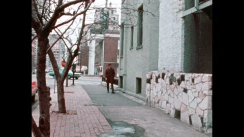 1970s: Man in glasses stops to lean against a wall and talk. Starts to cross the Stock Footage 241434980