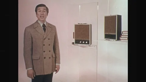 1970s: Man next to radios, talks into camera. Radios. Dissolve, close up pan of Video stock 75962142