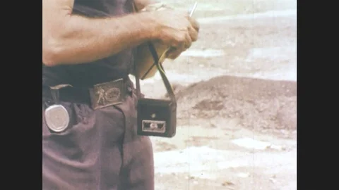 1970s: Man picks up shell. Man weaves yellow string through and around shell. Stock Footage