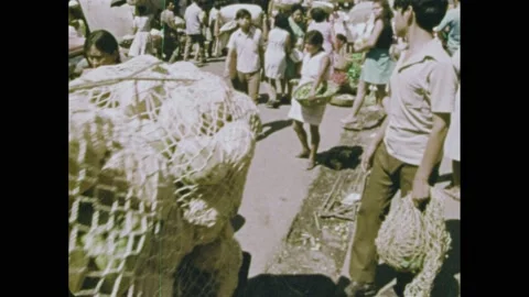1970s: Man pulling cart full of round objects in netting. People sitting in Stock Footage 164544392