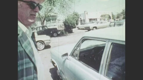 1970s: Man pushes car door shut. Car drives by. Man smiles and speaks. Man Stock Footage
