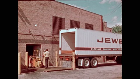 1970s: Man pushing pallet of boxes from truck. Truck backing up to warehouse. Video stock 239106479
