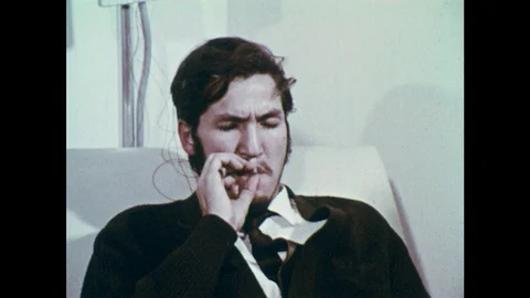 1970s: Man smokes joint on couch. Men smoke marijuana on couch. Inner city Stock Footage 102005111