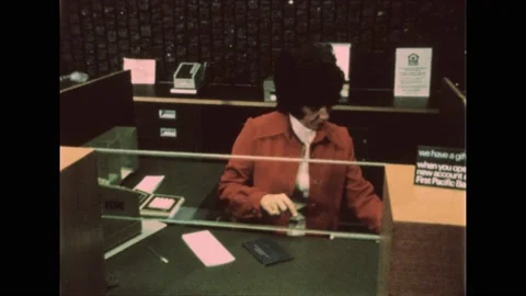 1970s: Man stands in front of teller window at bank. Bank teller counts out Stock Footage 194490643