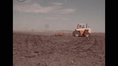 1970s: Man in tractor pulls disc harrow across dirt in farm field.  Wheat plants Stock Footage 154699779