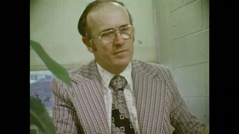 1970s: Man wears glasses. Man holds poster. Man speaks. Man behind books. Man Stock Footage