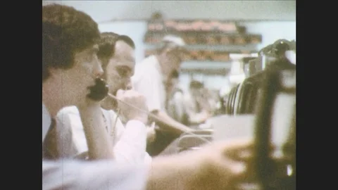 1970s: Men sit at cubicles, talk on phone, look at stock ticker. Trading room Stock Footage