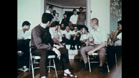 1970s: Men sit on door stoop and talk. Man talks to woman and boy on sidewalk.  Stock Footage 102005243