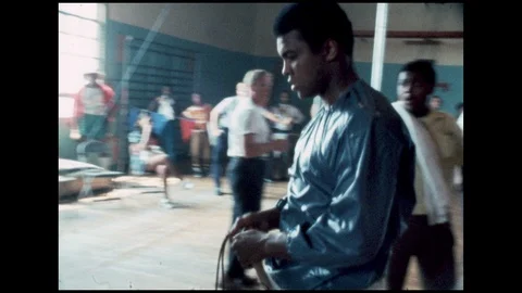 1970s: Muhammad Ali walks around gym, starts jumping rope. Men take photographs. Stock Footage