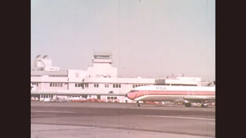 1970s: psa airplane taxis past airport terminal. woman talks on microphone Stock Footage