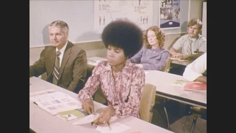 1970s: Students sit at tables in classroom. Women sit on lawn at campus. Men and Видео 80066011