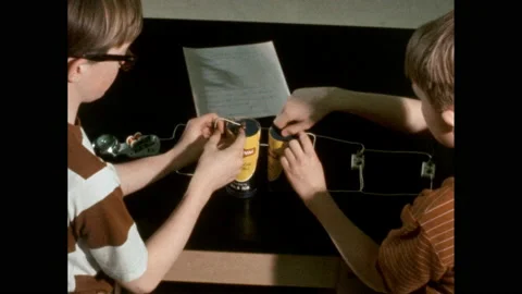 1970s: Two boys attach two batteries to a parallel circuit which contains Video stock 163452053