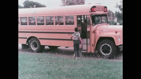 1970s: Two boys wait on grass as school bus pulls up, they get on. Boys sit on Stock Footage 224312821