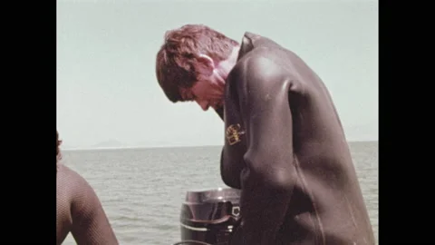 1970s: Two men with mustaches prepare scuba-gear on a rubber motorboat. They zip Stock Footage 150351920