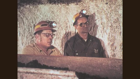 1970s: Two mine workers watch conveyor belt transport coals. Mine worker Stock Footage 79463823