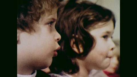 1970s: UNITED STATES: children watch commercials on television. Boy eats sweets Stock Footage