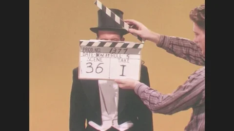 1970s: UNITED STATES: clapper loader stands with clapper board. Magician speaks Stock Footage 79047133