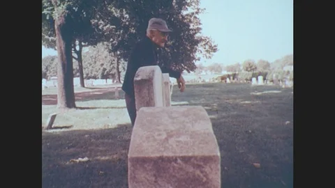 1970s: United States: Stone Cross At Cemetary. Man Walks To Grave Stone. Close Stock Footage