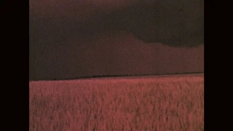 1970s: Wall cloud and lightning in distance of storm, beyond farms. Tornado Stock Footage 121588119