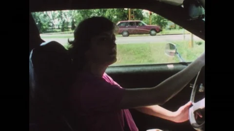 1970s: Woman drives car. Woman looks to left. Woman makes U-turn. Car drives on Stock Footage