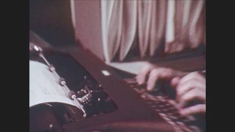 1970s: Woman quickly types on typewriter while reading paper. Office with men Stock Footage