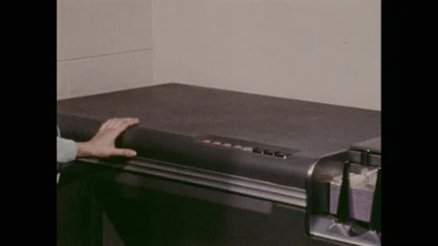1970s: Woman stands at processing machine in office. Parts inside machine move. Stock Footage 157935419