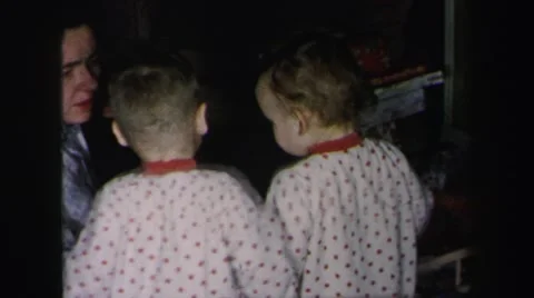 1972: two toddlers in matching pajamas looking at new toys with mother helping Stock Footage