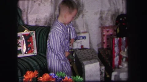 1974: a little boy in purple striped pajamas retrieving a gift and opening it up Stock Footage