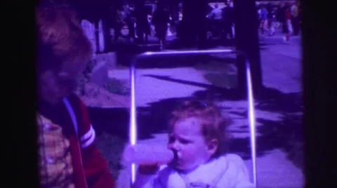 1974: redhead big brother pushing around kid sister in stroller on sidewalk Stock Footage