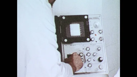 1980s: Man adjust knobs on machine. Woman lays in bed. Man places electroes on 스톡 동영상 94465614