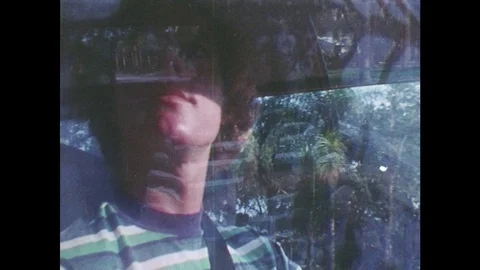 1980s: man in striped shirt drives car and looks around at suburban neighborhood Stock Footage