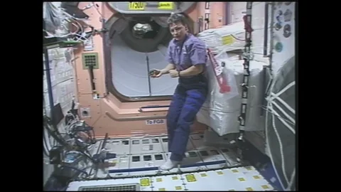 1990s: Astronaut plays with yo-yo in zero gravity on space station. Woman points 스톡 동영상 128213252