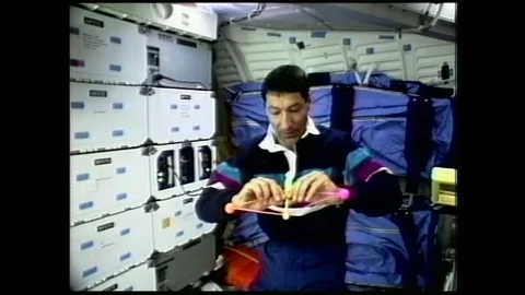 1990s: astronaut in zero gravity releases and spins clacker ball toy in air Stock Footage 129277852