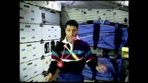 1990s: astronaut in zero gravity releases and spins clacker ball toy in air, it Stock Footage 129277854