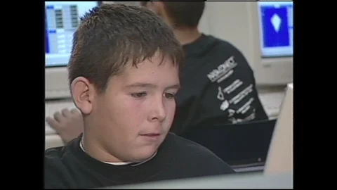 1990s: Boy sits at computer in room with other students at computers. Teacher 動画素材 120487214