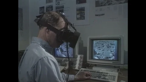 1990s: Man looks through virtual reality goggles in front of two computer Stock Footage 104994700