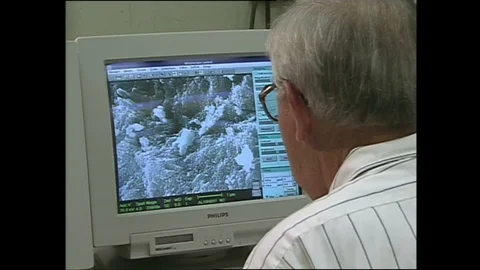 1990s: Man sitting at computer, zoom in on screen. Magnified images of microbes. 動画素材 129568980