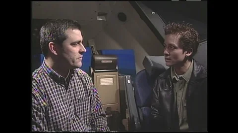 1990s: Two men sit in seats in plane, talking. Looking out window of airplane in Stock Footage 120488556